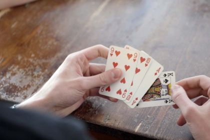 Hand die kaarten vasthoudt tijdens een potje toepen aan een houten tafel
